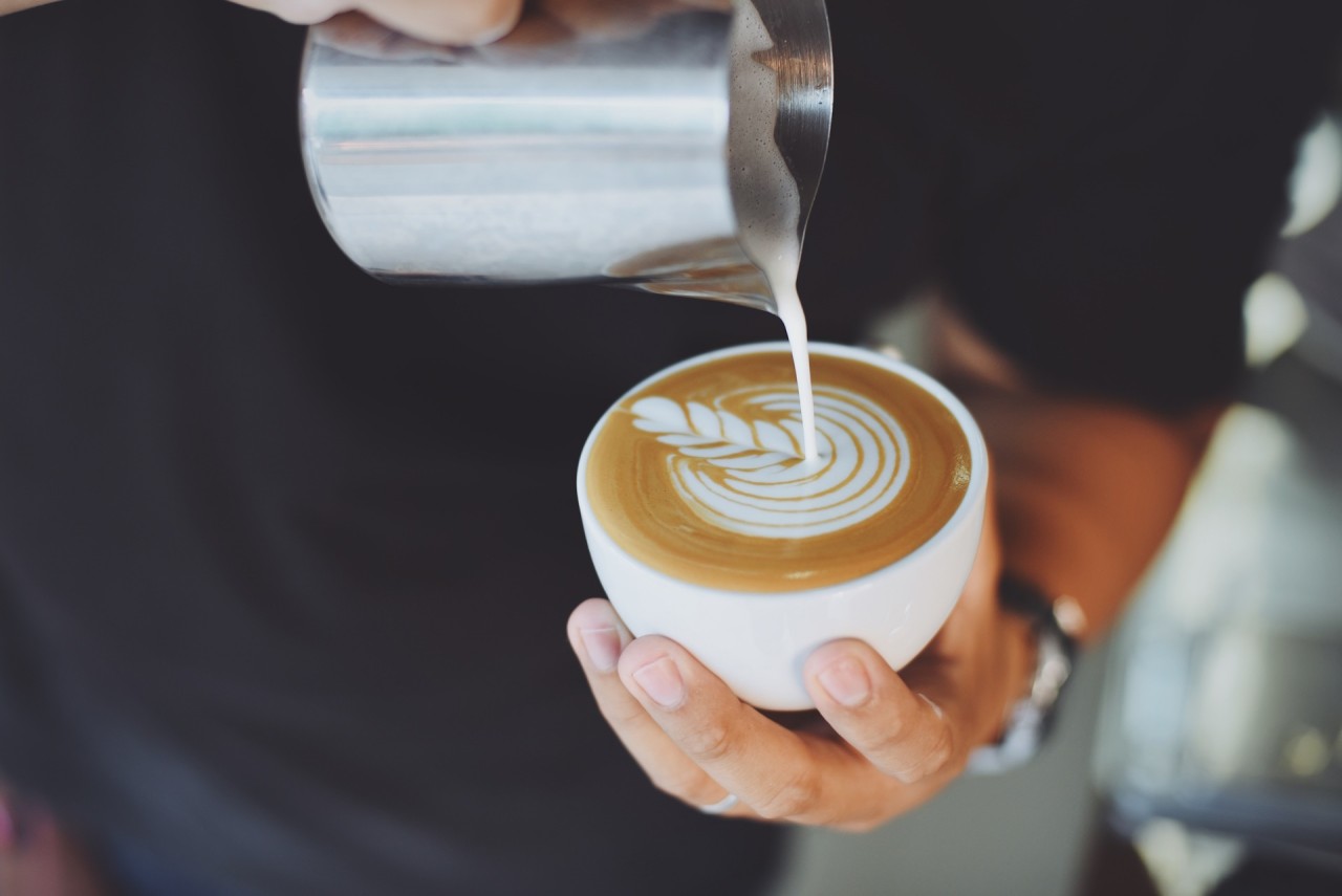 Person dient eine Tasse Kaffee mit einem Metall-Krug